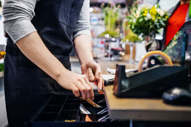03-minijob-mit-verdienstgrenze3  Ein Mitarbeiter eines Blumenladens legt Geld in die Geschäftskasse.