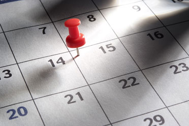 10a  Rote Reißzwecke auf einem Papierkalender.