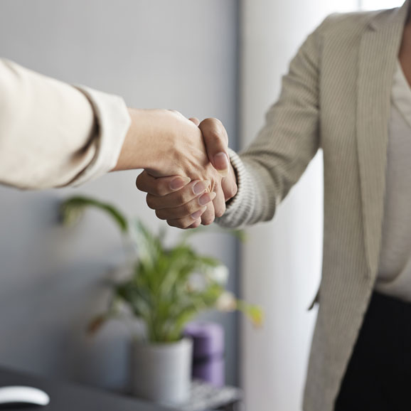 Arbeit auf Abruf1  Zwei Frauen schütteln sich die Hände im Büro. Dargestellt sind nur die Arme und der Oberkörper einer der Frauen.