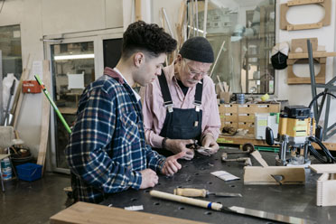 20-sonderfaelle1  Arbeiter einer Holzwerkstatt bereitet den Pflaster für einen Praktikanten vor, der sich bei der Arbeit den Finger geschnitten hat.