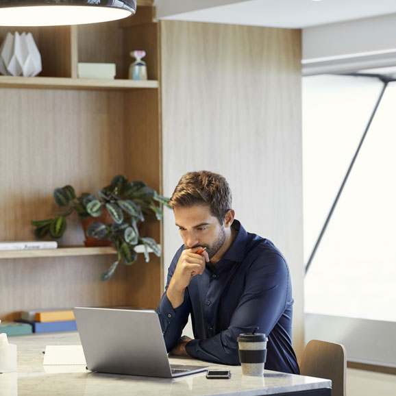 Junger weißer Mann sitzt konzentriert vor dem Laptop in einem hellen, modernen Büro. 