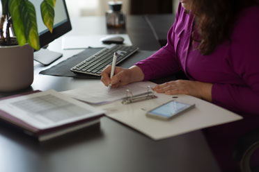 Eine Frau sitzt an ihrem Tisch im Büro und füllt ein Papierdokument aus. 