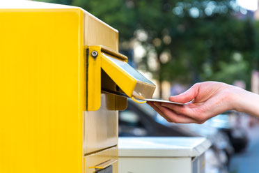 40-halbjahresscheck1  Eine Person schiebt einen Brief in einen gelben Briefkasten.